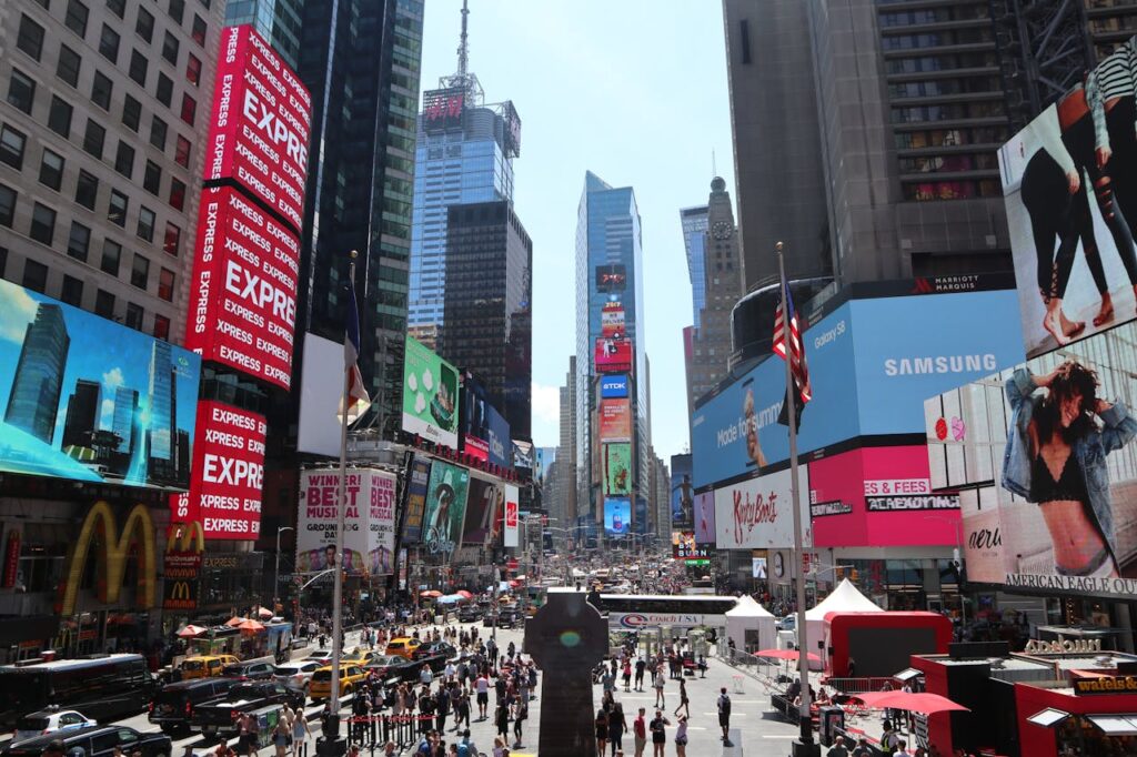 Bustling Times Square in NYC with billboards, crowds, and city life on a sunny day.
